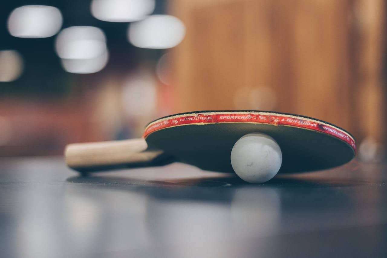 Close-up of a ping pong paddle and ball on a table with an artistic bokeh background, indoors.